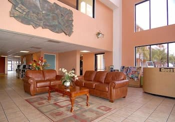 A cozy hotel lobby features plush leather sofas arranged around a wooden coffee table, set against a tiled floor and adorned with vibrant floral arrangements, creating a welcoming atmosphere ideal for travelers seeking relaxation.