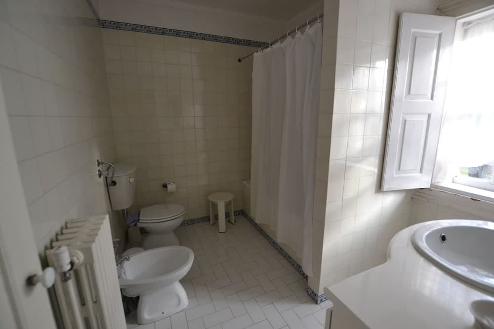 A bright, tiled bathroom with white fixtures, a bidet, a shower curtain, and natural light from a window creates a clean and functional space ideal for travelers seeking comfort in accommodations.