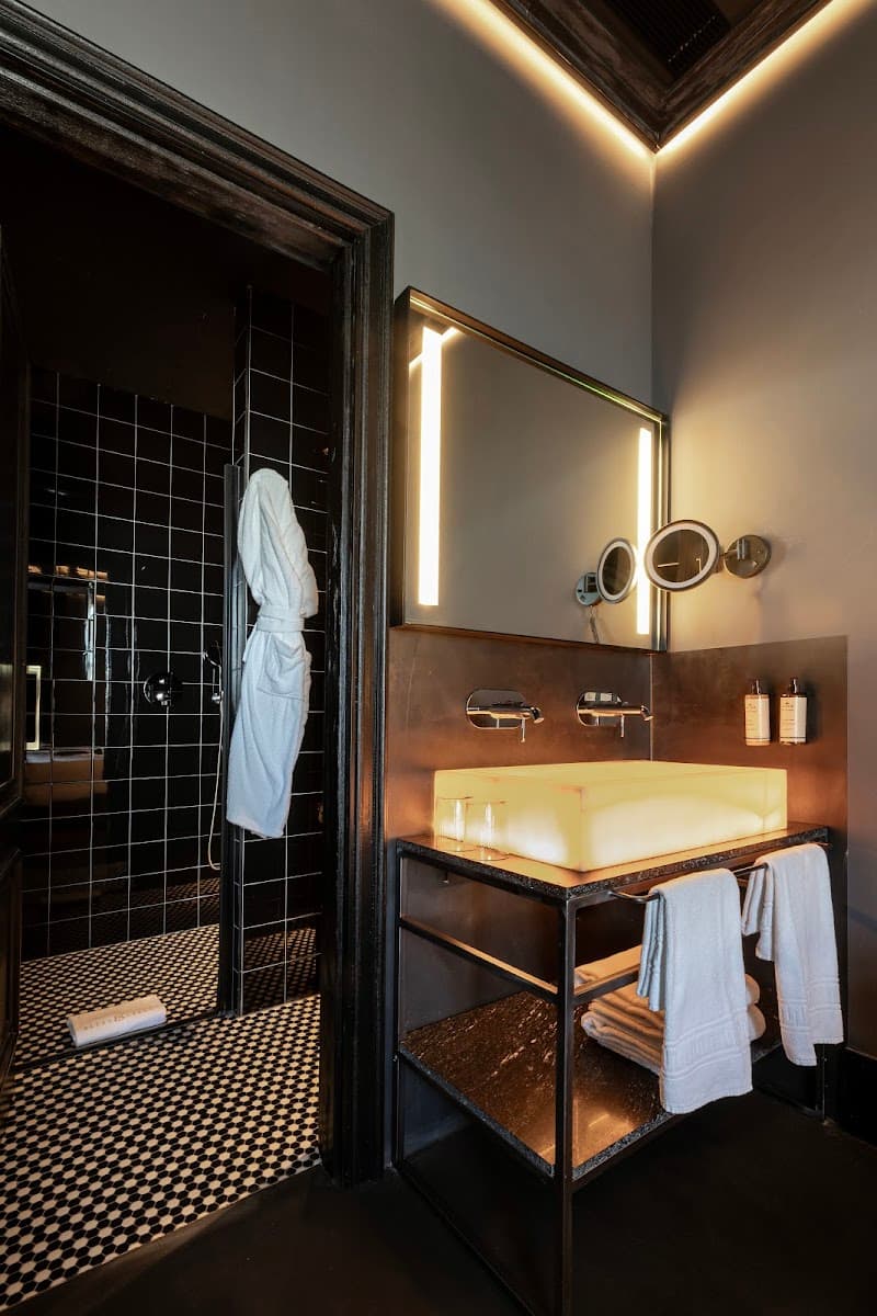 A luxurious hotel bathroom in Sevilla's historic center features a sleek sink with ambient lighting, a walk-in shower with black tiled walls, and neatly arranged towels, ideal for travelers seeking comfort and style.