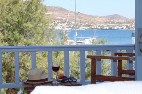 A serene balcony view overlooking a picturesque coastal town with sailboats on the water, featuring a straw hat, sunglasses, and a glass of wine, perfect for a relaxing seaside getaway.