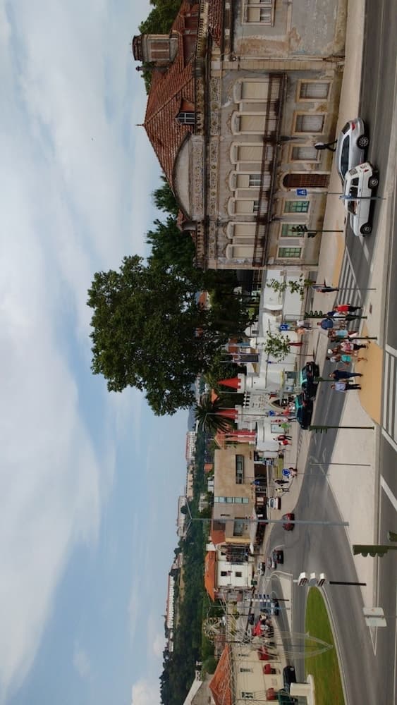 A vibrant European town square features historic architecture with ornate facades, bustling pedestrians, and parked cars under a partly cloudy sky, ideal for cultural exploration and leisurely strolls.