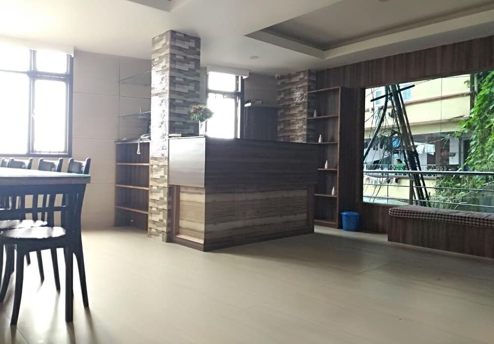 A cozy indoor lounge area features a wooden reception desk, bookshelves, and large windows overlooking greenery, ideal for travelers seeking a quiet retreat or business meeting space.