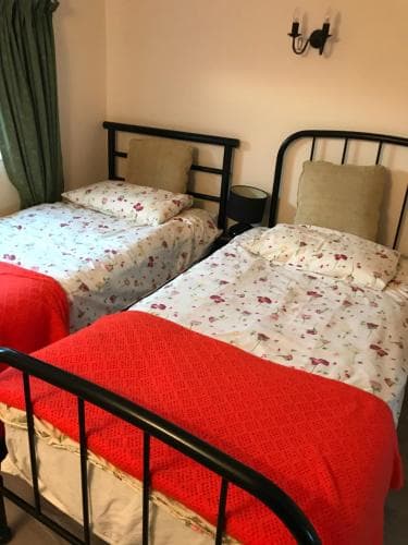 A cozy guesthouse room features two single beds with floral bedding and a red throw, set against soft beige walls with a green curtain, ideal for budget travelers seeking comfort.