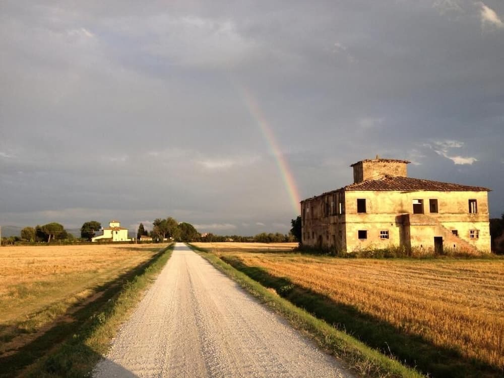 A serene rural landscape features a gravel path leading past an abandoned stone building under a dramatic sky with a vibrant rainbow, ideal for tranquil countryside exploration.