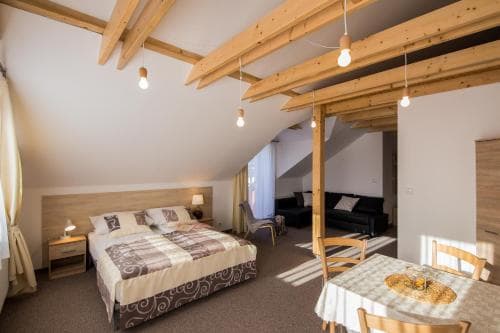 A cozy attic-style bedroom with wooden beams, a neatly made bed, and a small dining area bathes in soft natural light, ideal for travelers seeking a charming and intimate retreat.