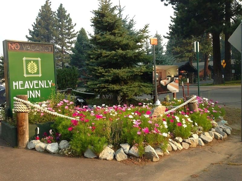 A vibrant garden of pink and white flowers adorns the entrance to the Heavenly Inn in South Lake Tahoe, creating a welcoming atmosphere with its lush greenery and rustic charm, ideal for travelers seeking a cozy retreat amidst nature.