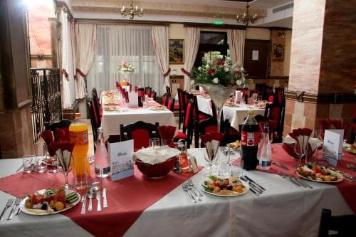 A cozy restaurant dining room with elegant tables set for a meal, adorned with red accents, floral arrangements, and warm lighting, ideal for travelers seeking an intimate dining experience.