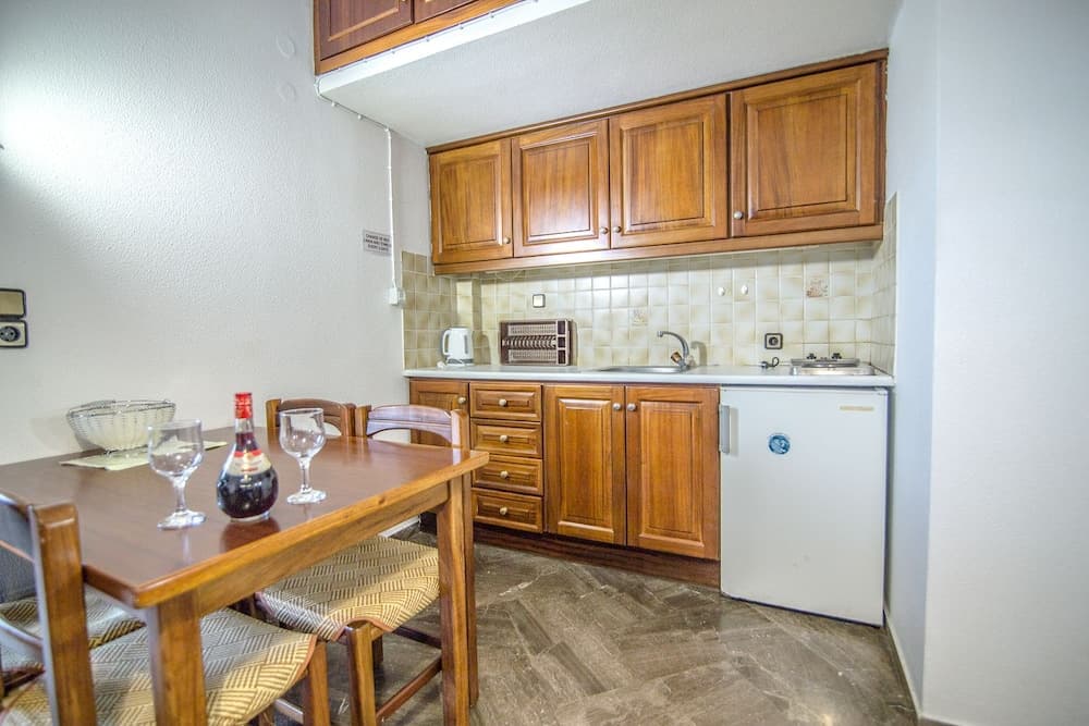 A cozy kitchenette with wooden cabinets, a small dining table set for two with wine glasses and a bottle, and essential appliances, ideal for travelers seeking self-catering accommodations in a compact space.