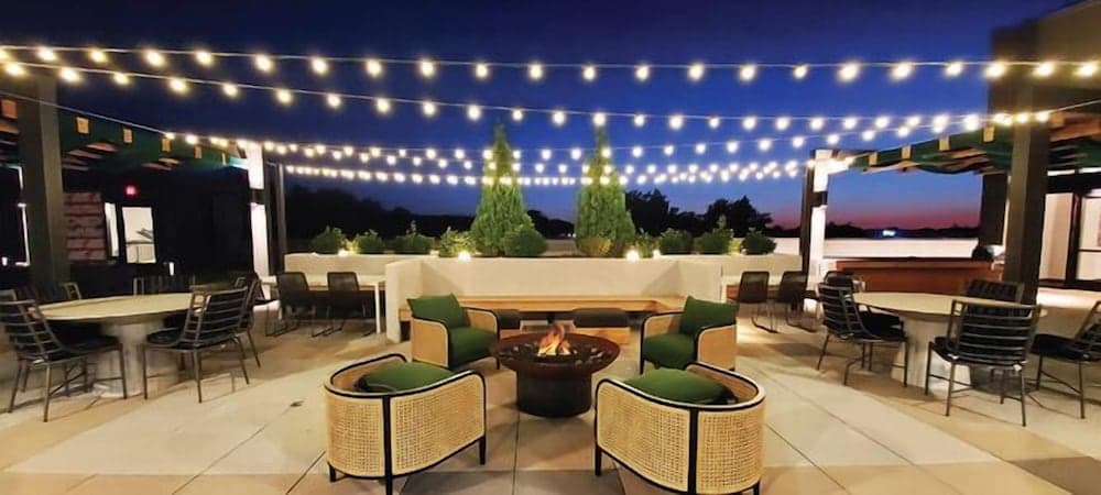 A cozy rooftop patio illuminated by string lights features comfortable seating around a fire pit, creating an inviting evening atmosphere perfect for social gatherings or romantic dates.