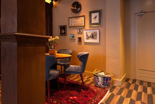 A cozy hotel lobby features warm lighting, a checkered floor, a vibrant rug, and eclectic wall art, creating an inviting atmosphere perfect for travelers seeking comfort and charm.