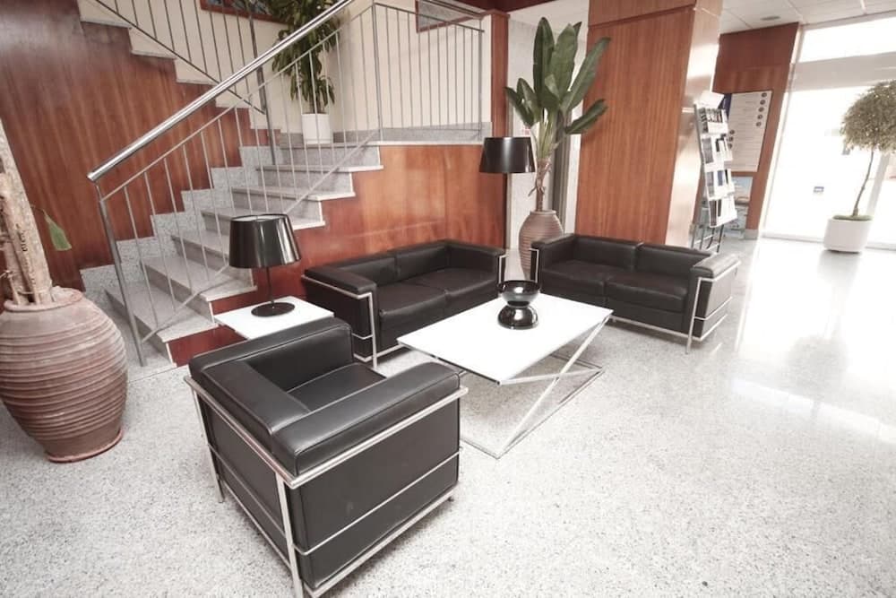 A modern, inviting hotel lobby features sleek black leather furniture, a staircase with metal railings, large potted plants, and a bright, airy atmosphere ideal for travelers seeking comfort and style.