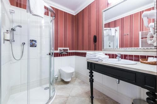 A cozy hotel bathroom features a glass-enclosed shower, a sleek black vanity with a white sink, neatly folded towels, and red-striped walls, ideal for travelers seeking comfort and style during their stay.