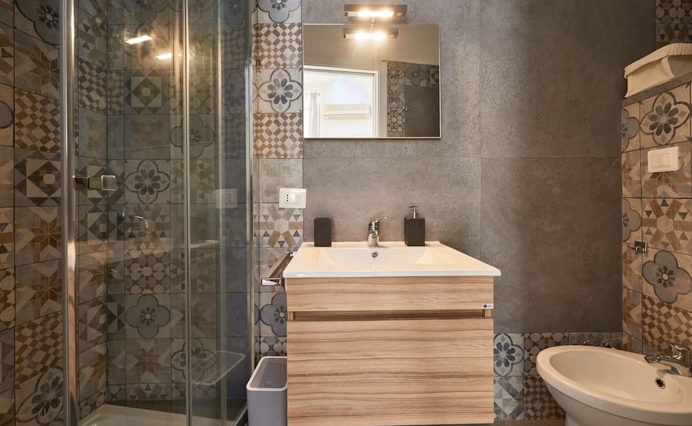 A modern bathroom features a sleek wooden vanity, patterned tiles, and a glass-enclosed shower, creating a stylish and functional space ideal for travelers seeking comfort and design in their accommodations.