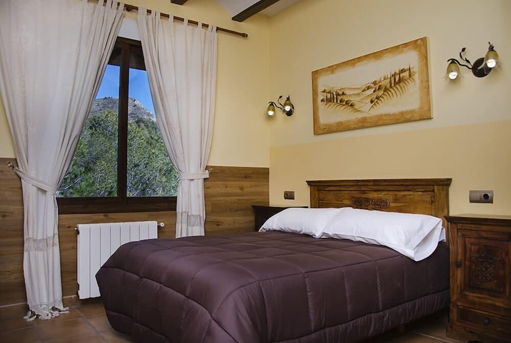A cozy bedroom with rustic wooden furniture, warm yellow walls, and a scenic mountain view through the window, ideal for travelers seeking a serene retreat in a countryside lodge.