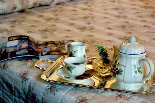 A cozy hotel room scene features a floral-patterned bedspread adorned with a golden tray holding elegant white tea set and a small green plant, evoking a serene and inviting atmosphere perfect for a relaxing getaway.