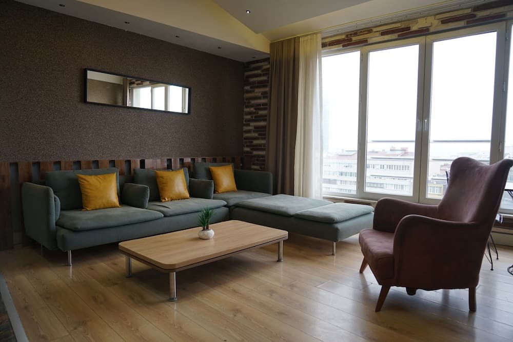 A cozy living room with modern furniture, large windows offering city views, warm lighting, and a minimalist decor creates an inviting atmosphere ideal for travelers seeking comfort in urban accommodations.