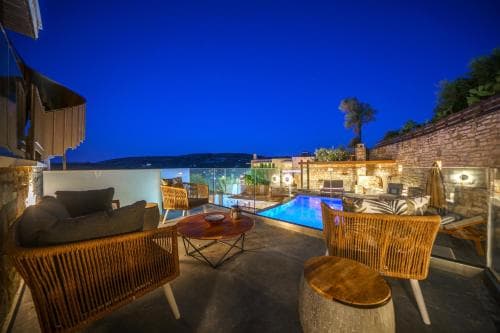 A serene rooftop terrace at dusk features cozy wicker furniture, a glowing pool, and a panoramic view, ideal for a luxurious vacation retreat.