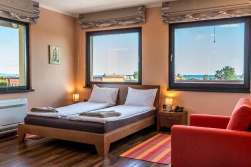A cozy hotel room with a serene ocean view through large windows, featuring a neatly made bed, warm lighting, and vibrant decor, ideal for travelers seeking relaxation by the seaside.