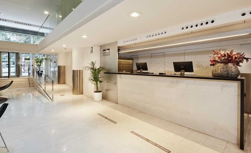 A modern hotel lobby in Barcelona's Eixample district features sleek marble floors, a polished reception desk adorned with decorative plants and vases, creating an inviting atmosphere ideal for travelers seeking comfort and style.