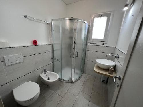 A modern, compact bathroom with tiled walls, a glass shower enclosure, bidet, sink, and toilet, exudes cleanliness and functionality, ideal for travelers seeking efficient accommodations.