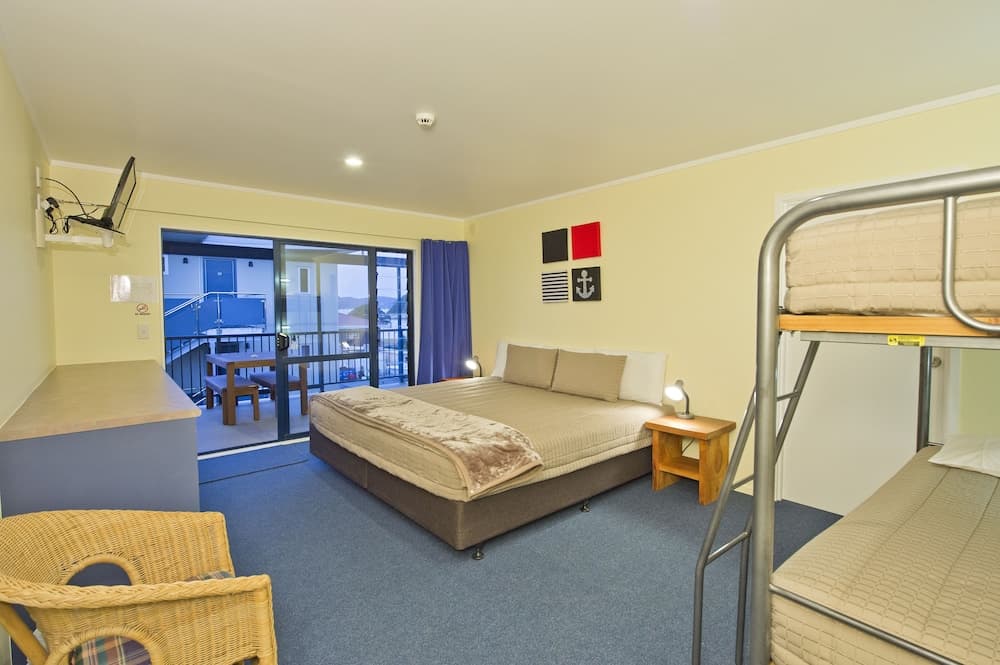A cozy hotel room with a queen bed, bunk beds, nautical-themed decor, and a balcony view offers a comfortable stay for travelers seeking relaxation and convenience.