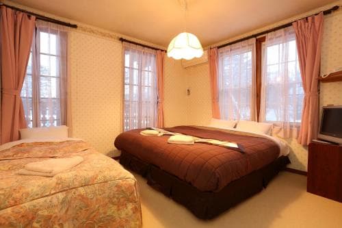 A cozy hotel room with two neatly made beds, soft pink curtains framing large windows, and a warm ambiance, ideal for travelers seeking comfort and relaxation.