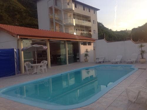 A serene evening at a cozy resort features a tranquil pool surrounded by lounge chairs, a glass-enclosed dining area, and a multi-story building, ideal for a relaxing vacation getaway.