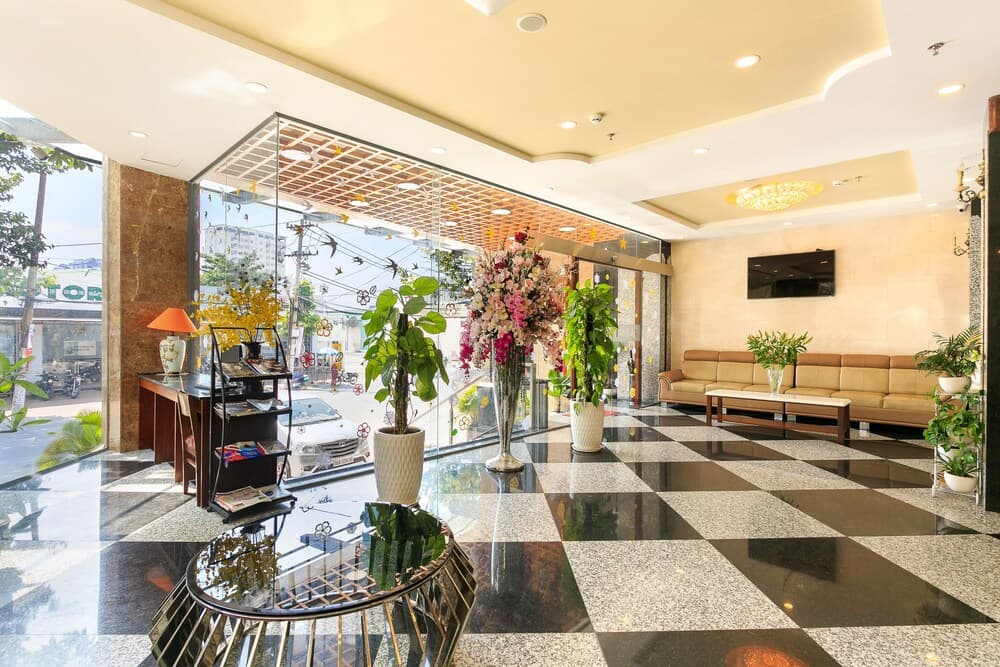 A bright and inviting hotel lobby features a glossy checkered floor, lush greenery, vibrant floral arrangements, and comfortable seating, ideal for travelers seeking a welcoming atmosphere during their stay.
