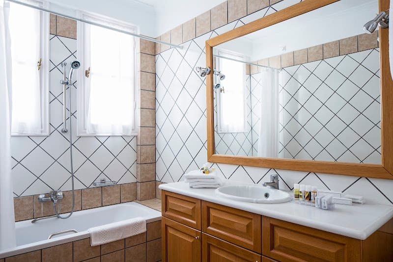 A cozy bathroom with tiled walls, wooden cabinetry, and natural light from a window offers a serene retreat at the Atlantis Hotel in Thira, Greece, ideal for travelers seeking comfort near cultural landmarks.