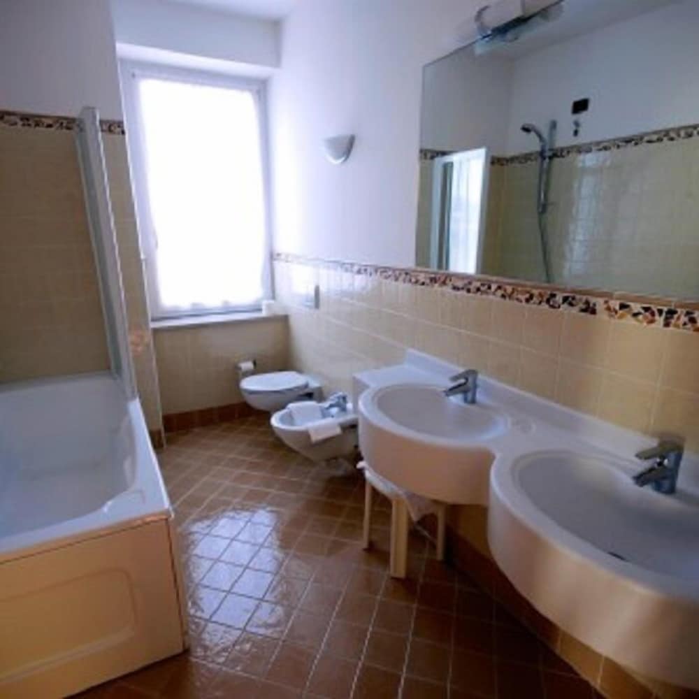 A bright, spacious bathroom with dual sinks, a bathtub, bidet, and tiled walls offers a clean and functional space ideal for travelers seeking comfort in accommodations.