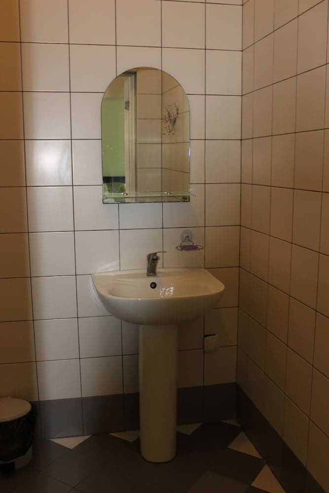A clean, tiled bathroom corner features a white pedestal sink under an arched mirror, with a geometric floor pattern, ideal for travelers seeking simple and functional accommodations.