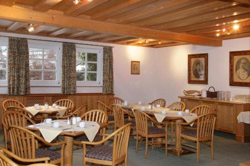 A cozy restaurant with wooden beams, patterned curtains, and neatly arranged tables creates a warm and inviting atmosphere, perfect for travelers seeking a comfortable dining experience.