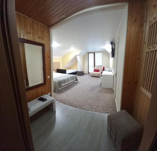 A cozy attic-style hotel room with wooden walls, a carpeted floor, and multiple beds offers a comfortable retreat for travelers seeking a quaint and inviting accommodation.
