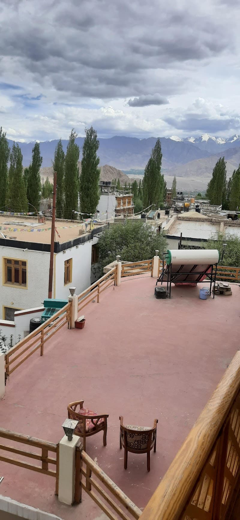 A serene rooftop terrace at Hotel Ladakh Inn offers breathtaking views of snow-capped mountains and lush greenery, perfect for travelers seeking tranquility and scenic vistas in Leh.
