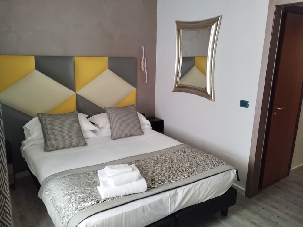 A cozy hotel room features a neatly made bed with a geometric-patterned headboard, a stylish mirror on the wall, and soft lighting, ideal for travelers seeking comfort and modern design.