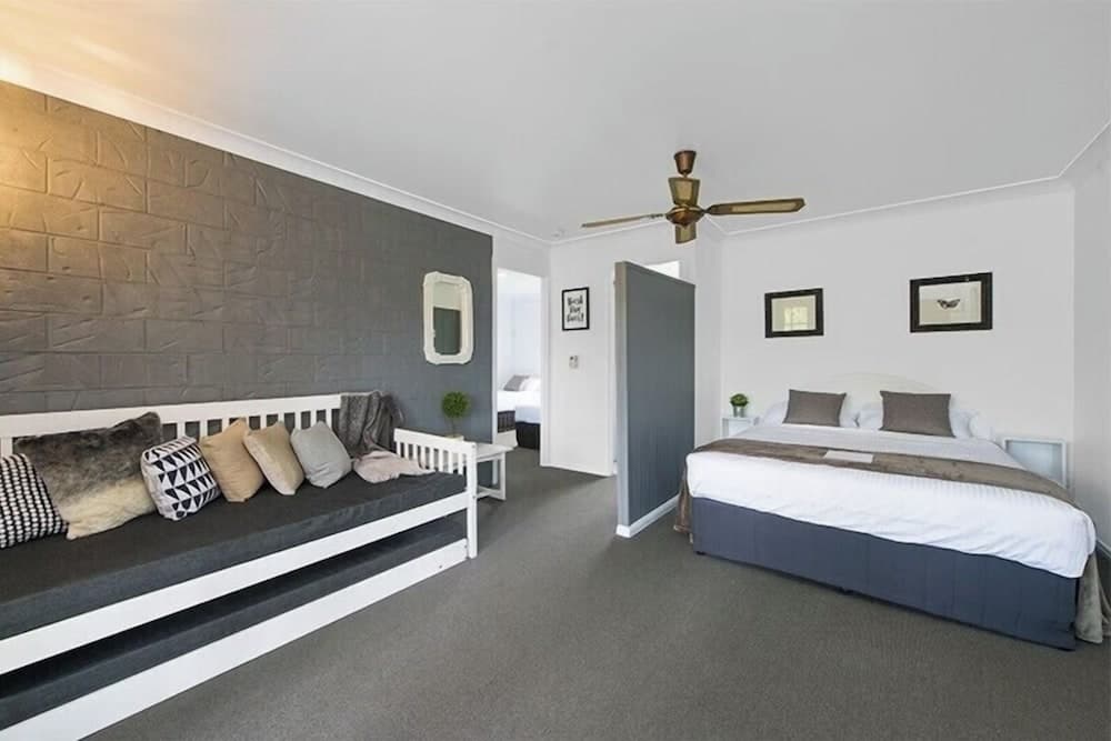 A cozy bedroom with a modern aesthetic features a gray brick accent wall, a comfortable daybed adorned with pillows, a neatly made bed, and tasteful decor, ideal for travelers seeking a serene and stylish accommodation.