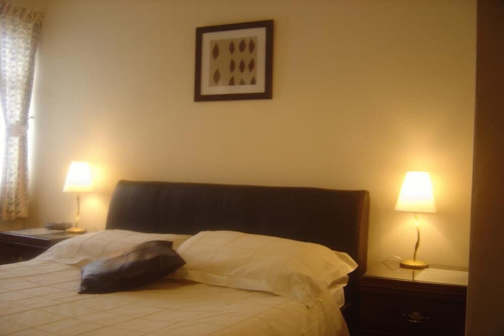 A cozy hotel bedroom features a neatly made bed with white linens, warm bedside lamps, and a framed artwork above the headboard, ideal for travelers seeking comfort and relaxation.