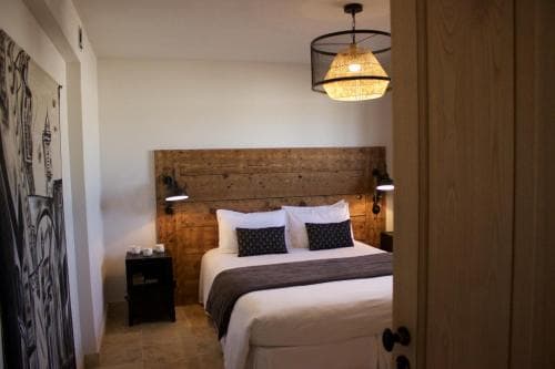 A cozy hotel room features a rustic wooden headboard bed, ambient lighting from a unique pendant lamp, and modern decor, ideal for travelers seeking comfort and style in their accommodations.