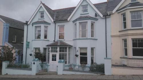 A charming pastel blue Victorian house with white trim and a quaint garden fence exudes a cozy, inviting atmosphere in a residential neighborhood, perfect for travelers seeking a picturesque stay.