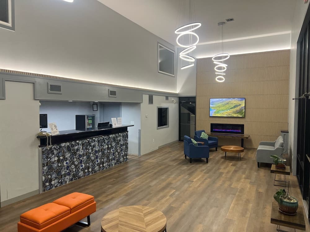 A modern hotel lobby features a sleek reception desk with a mosaic design, cozy seating areas, a fireplace, and contemporary lighting, creating a welcoming atmosphere ideal for travelers seeking comfort and style.