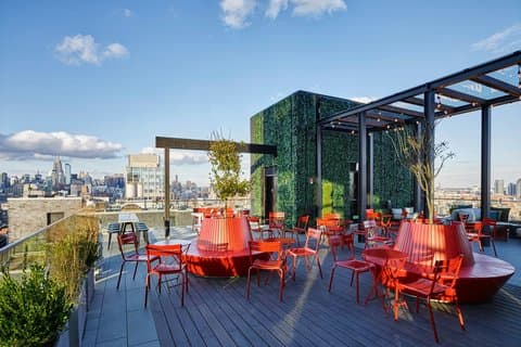 A vibrant rooftop terrace at citizenM New York Bowery features modern red seating, lush green walls, and panoramic city views, ideal for travelers seeking a stylish urban retreat.