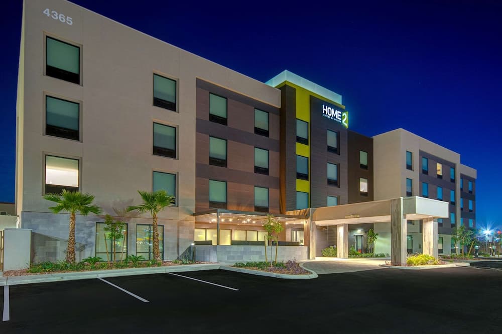 A modern hotel illuminated at night features a welcoming entrance, palm trees, and a well-lit parking area, ideal for travelers seeking comfortable accommodations in an urban setting.