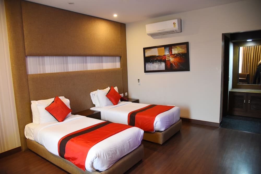 A cozy hotel room features two neatly made beds with red accents, a modern abstract painting on the wall, and a sleek wooden floor, ideal for travelers seeking comfort and style.
