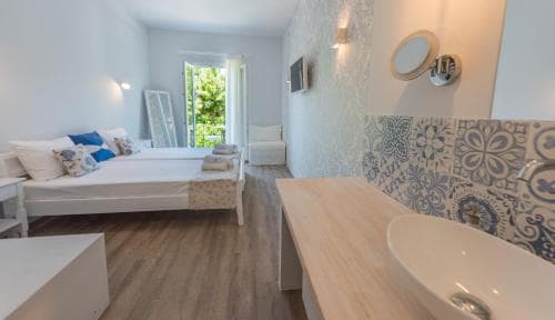 A cozy bedroom with wooden floors, white furnishings, and blue patterned tiles exudes a serene atmosphere, perfect for travelers seeking relaxation in a stylish retreat.