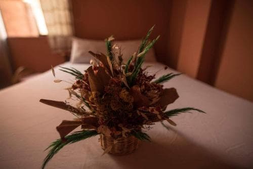 A cozy hotel room exudes warmth with a rustic wicker basket filled with dried flowers and greenery on a neatly made bed, perfect for travelers seeking a serene and inviting atmosphere.