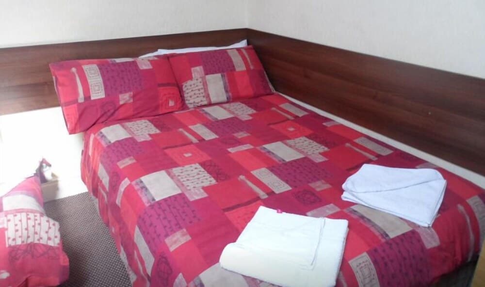 A cozy hotel room features a neatly made bed with a vibrant red patchwork quilt, white towels, and a wooden headboard, ideal for travelers seeking comfort and simplicity.