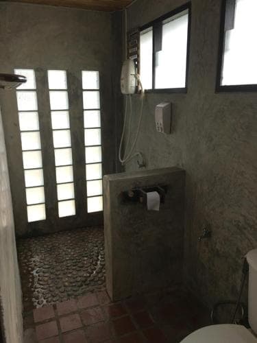 A rustic bathroom with textured walls, pebble flooring, and frosted glass windows exudes a serene ambiance, ideal for travelers seeking unique accommodations with natural elements.