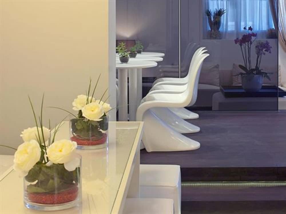 A serene modern lounge features sleek white chairs, minimalist tables adorned with vibrant flowers, and a cozy seating area, ideal for travelers seeking a tranquil retreat during their journey.
