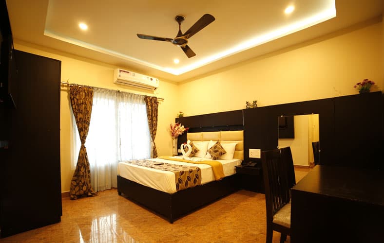 A cozy hotel room in Rameshwaram, Tamil Nadu, features warm lighting, a neatly made bed with decorative pillows, a dining area, and a serene ambiance ideal for travelers seeking comfort and relaxation.