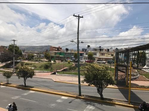 A vibrant urban street scene with colorful buildings, lush greenery, and a modern pedestrian bridge under a partly cloudy sky, ideal for city exploration and cultural immersion.